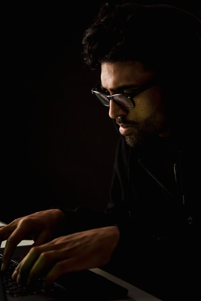 A man in a dark room intently typing on a laptop, highlighting cyber technology themes.
